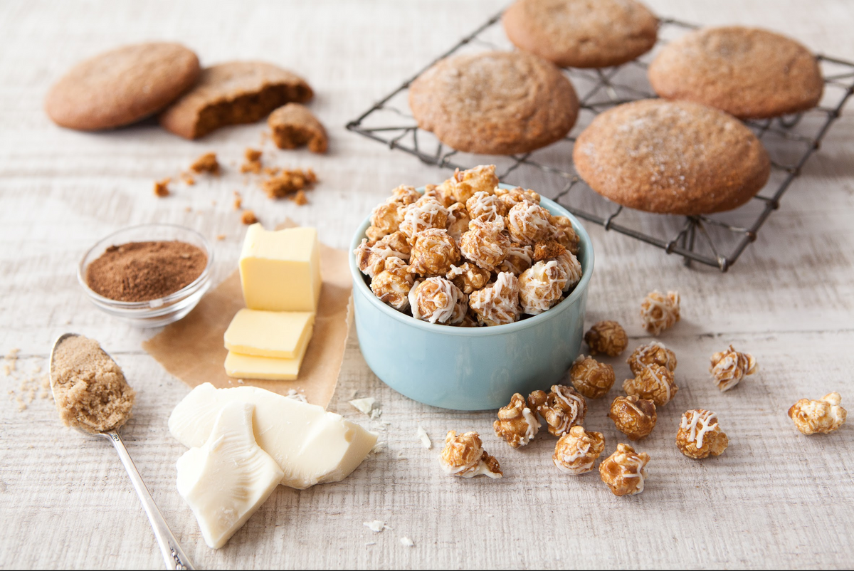 Caramel popcorn in a blue bowl with cookies on a cooling rack and ingredients on a wooden surface.